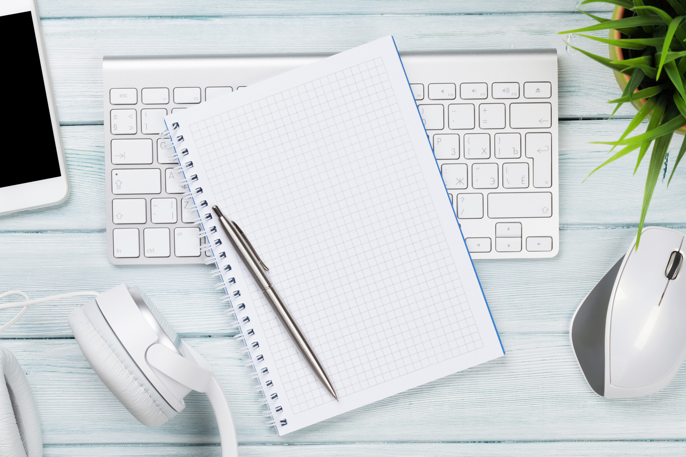 Wooden desk with notepad, headphones, pc, phone and plant